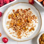 A bowl of high protein granola on top of yogurt, with raisins mixed in.