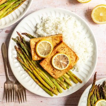 A plate of cooked asparagus, white rice, and lemon pepper tofu, topped with lemon slices.