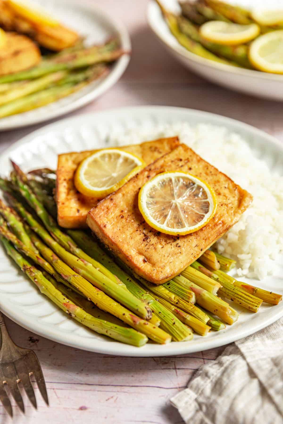 A plate of cooked asparagus, white rice, and lemon pepper tofu, topped with lemon slices.