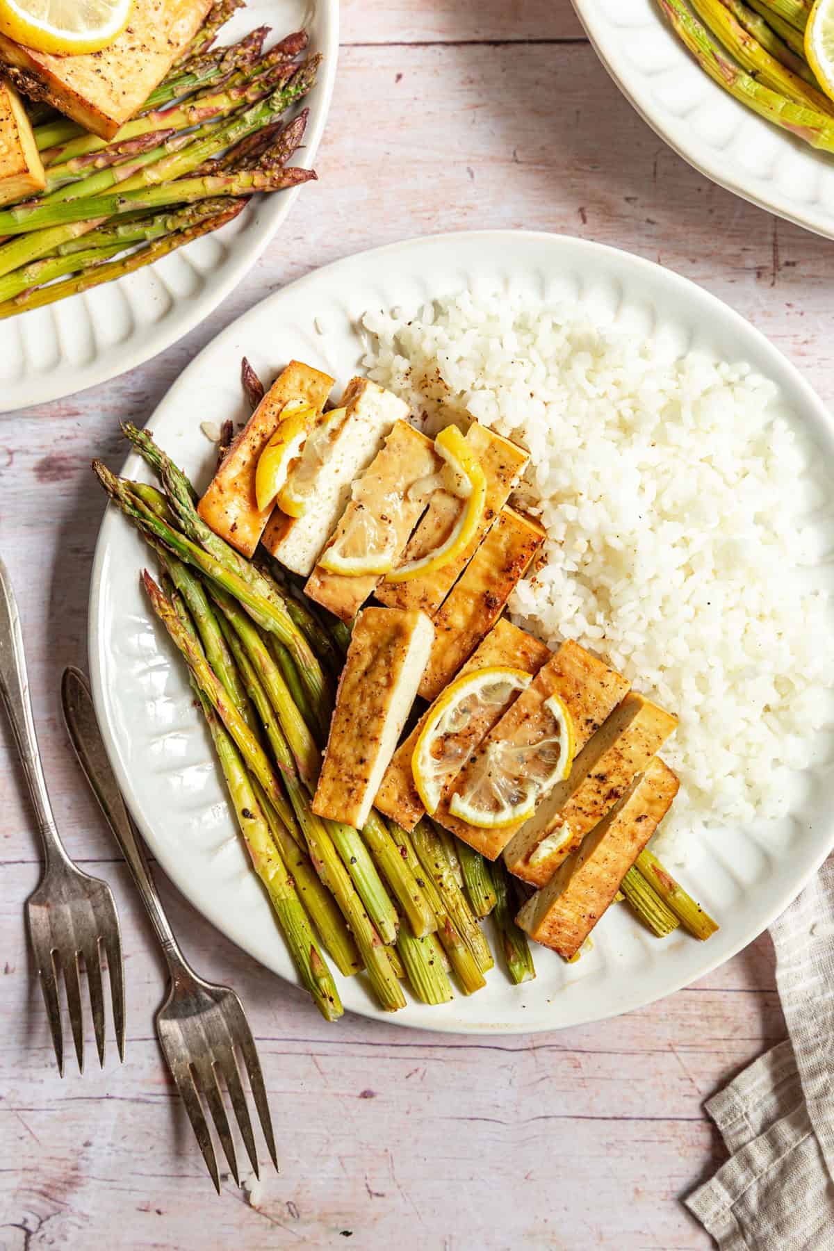 A plate of lemon pepper tofu sliced over rice and asparagus.