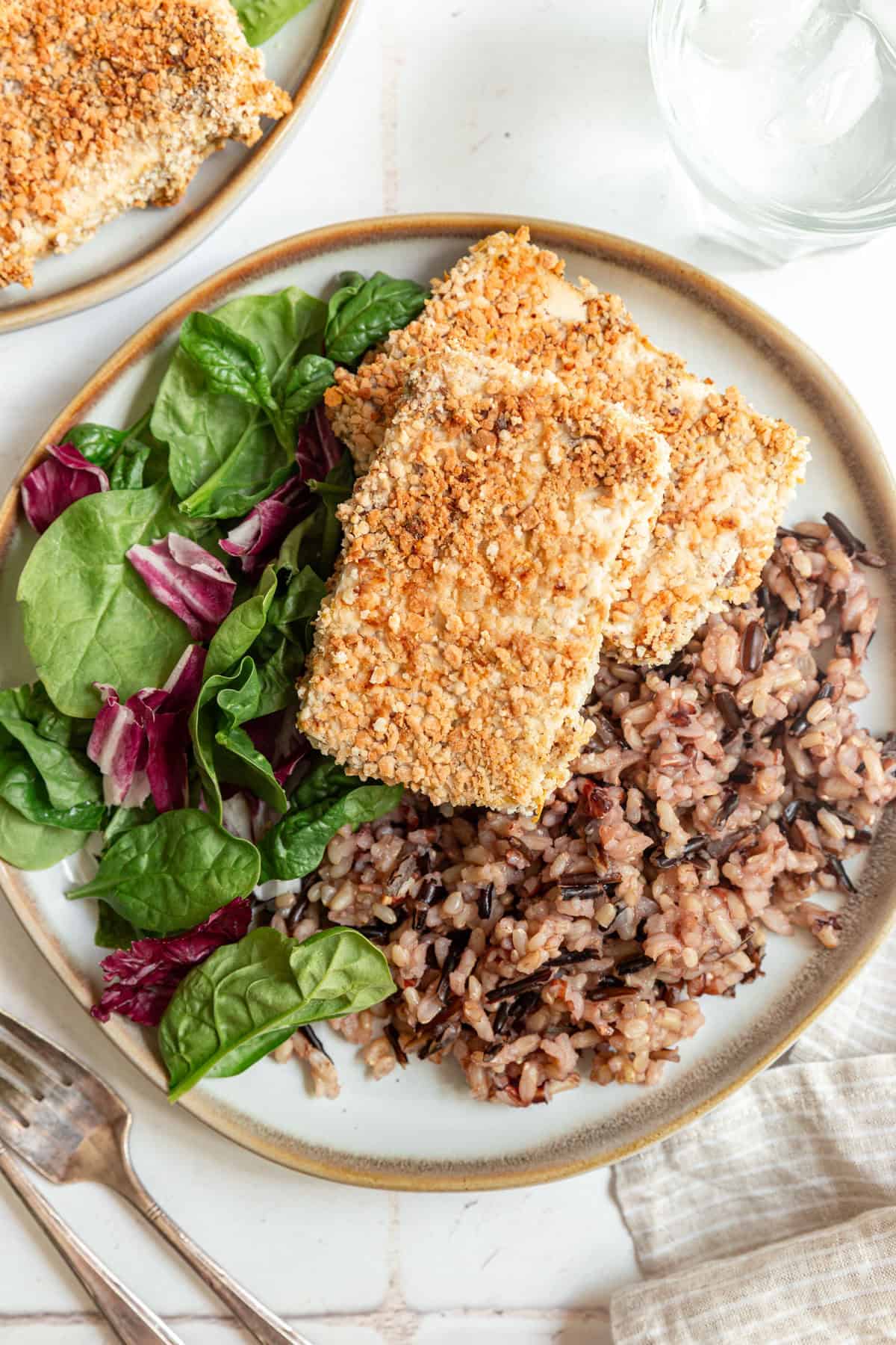 Two slabs of Panko Crusted Tofu on a plate with brown rice and salad.