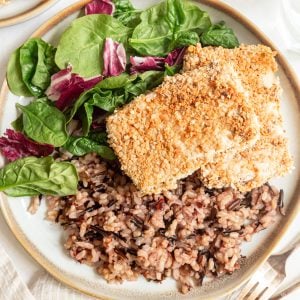 Two slabs of Panko Crusted Tofu on a plate with brown rice and salad.