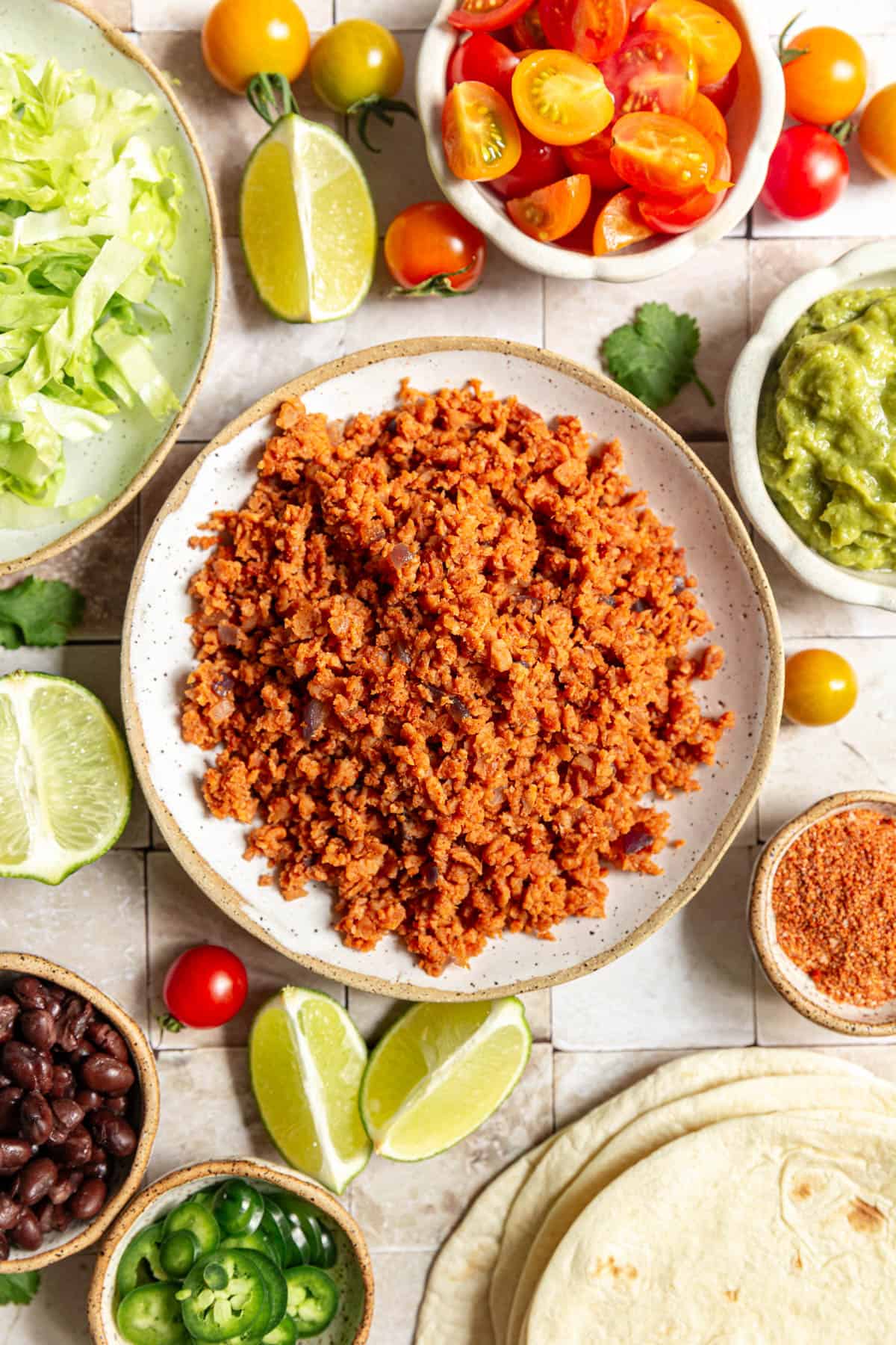 A bowl of TVP taco meat surrounded by bowls of toppings.