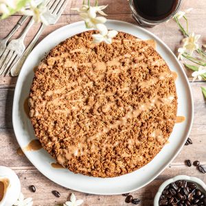 Vegan coffee cake on a large plate, drizzled with glaze, ready to slice.