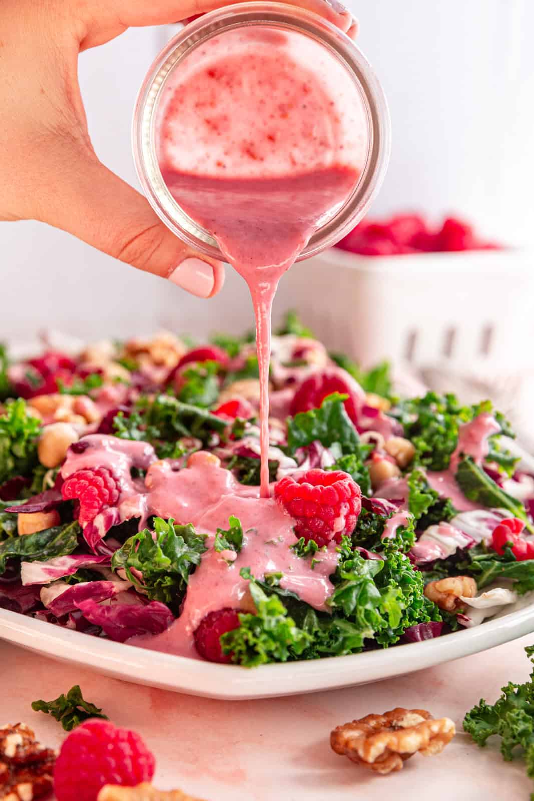 Raspberry Walnut Kale Salad being drizzled with Raspberry Vinaigrette.