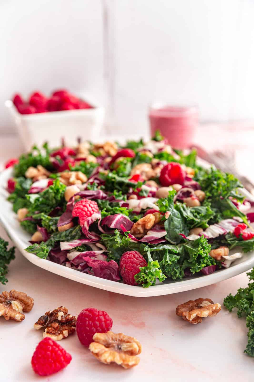 Raspberry Walnut Kale Salad surrounded with raspberries and walnuts.