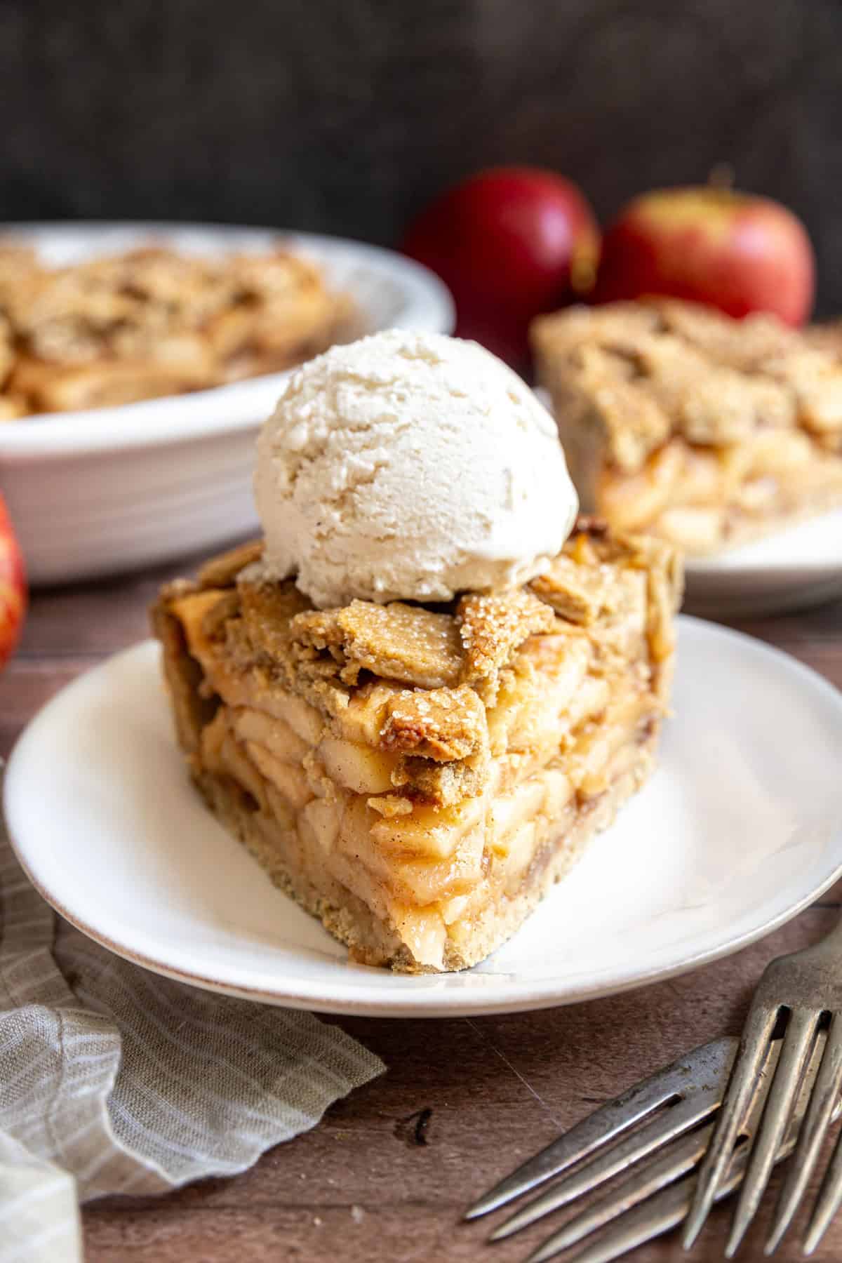 A slice of gluten free vegan apple pie on a plate, with a scoop of ice cream on top.