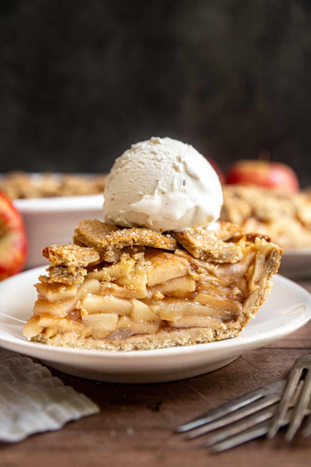 A slice of gluten free vegan apple pie on a plate, with a scoop of ice cream on top.