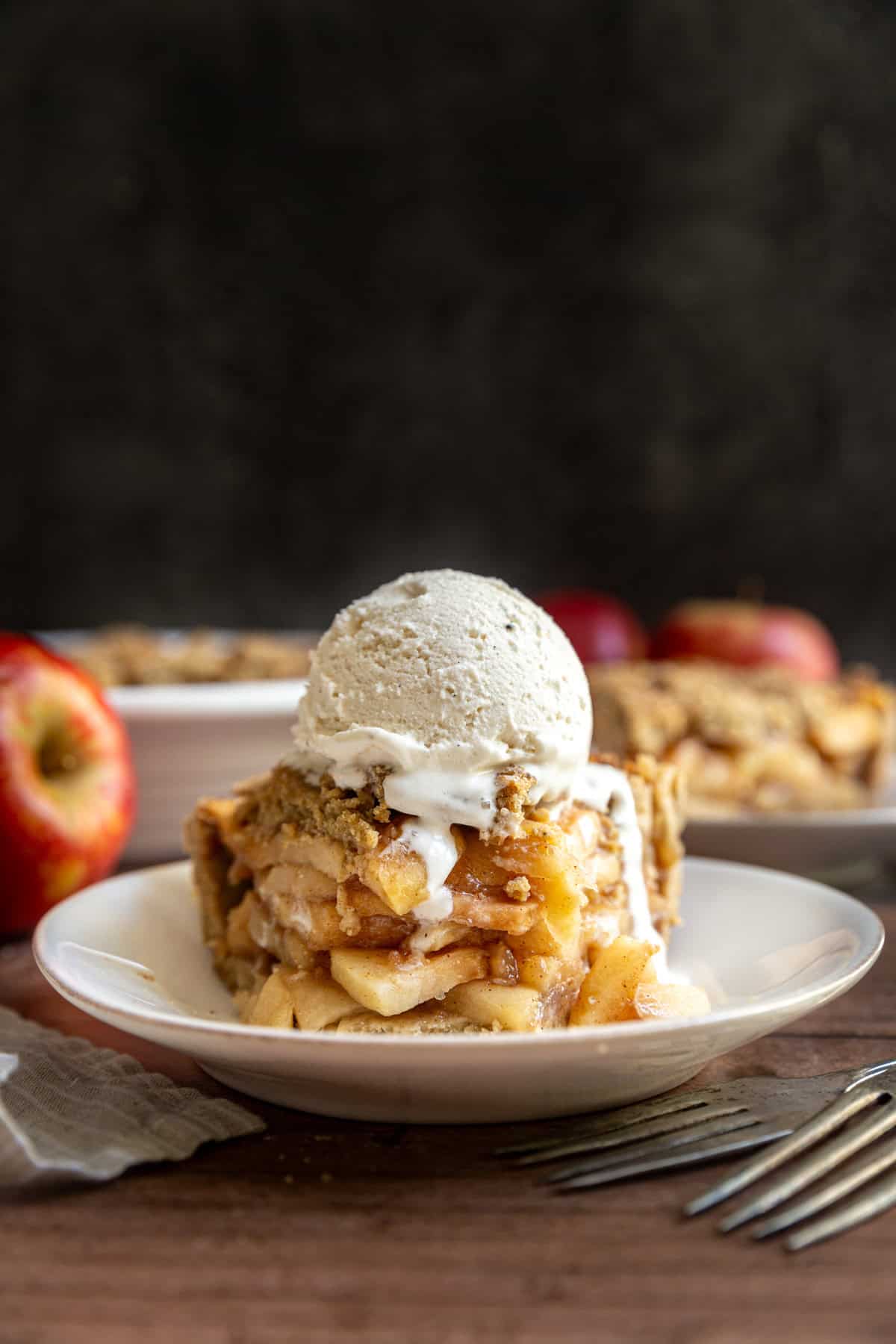 A slice of gluten free vegan apple pie on a plate, with a scoop of ice cream on top, and a bite taken out.