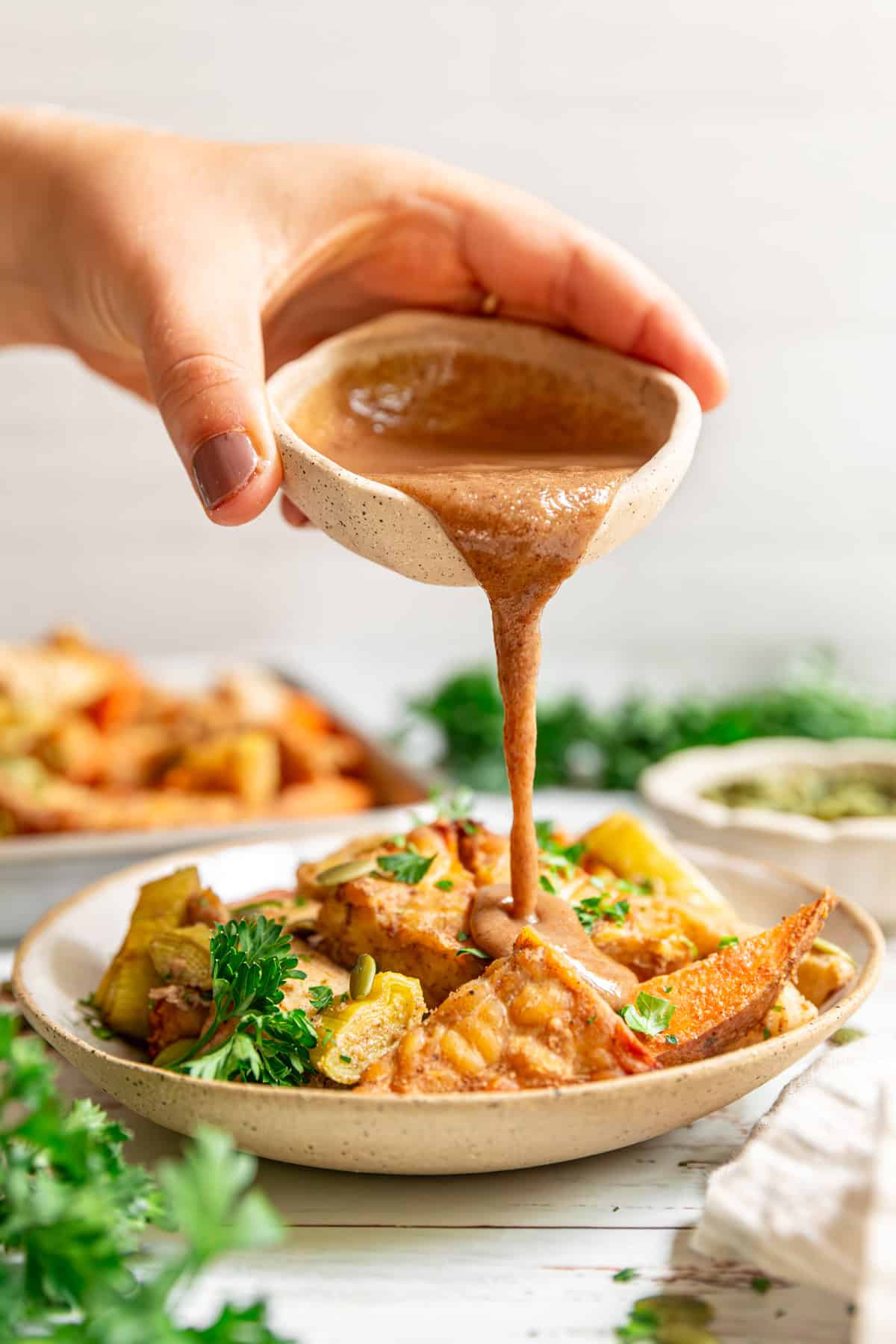 Drizzling tahini sauce on a bowl of sheet pan tempeh and fall vegetables.