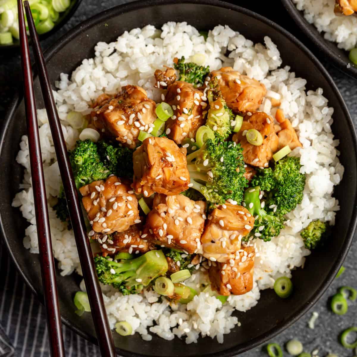 A bowl of teriyaki tempeh served on top of rice, with chopsticks.