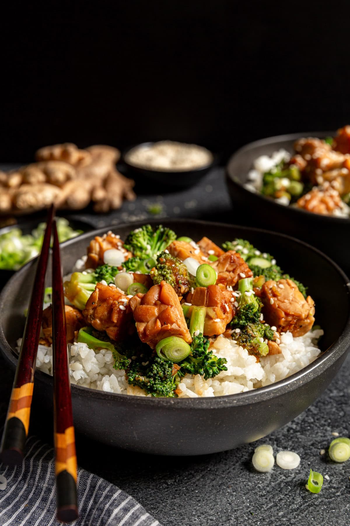 A bowl of teriyaki tempeh served on top of rice, with chopsticks.