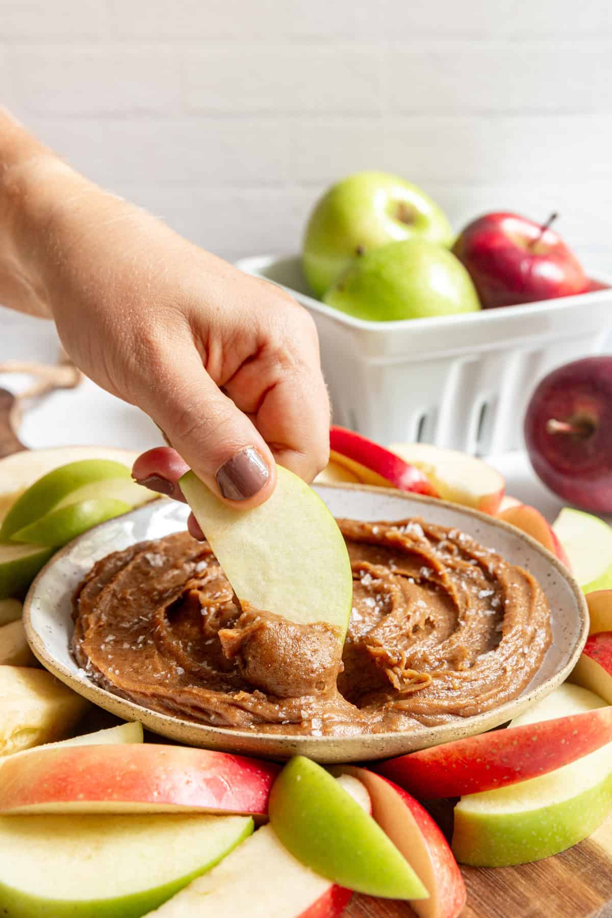 A person dipping an apple into a bowl of Vegan Date Caramel Sauce.