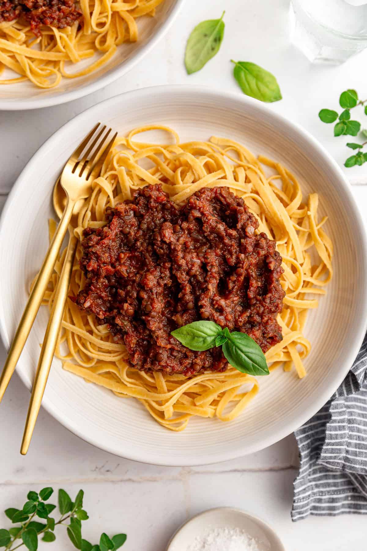 A bowl of vegan lentil bolognese on top of linguine pasta, with a garnish of basil.