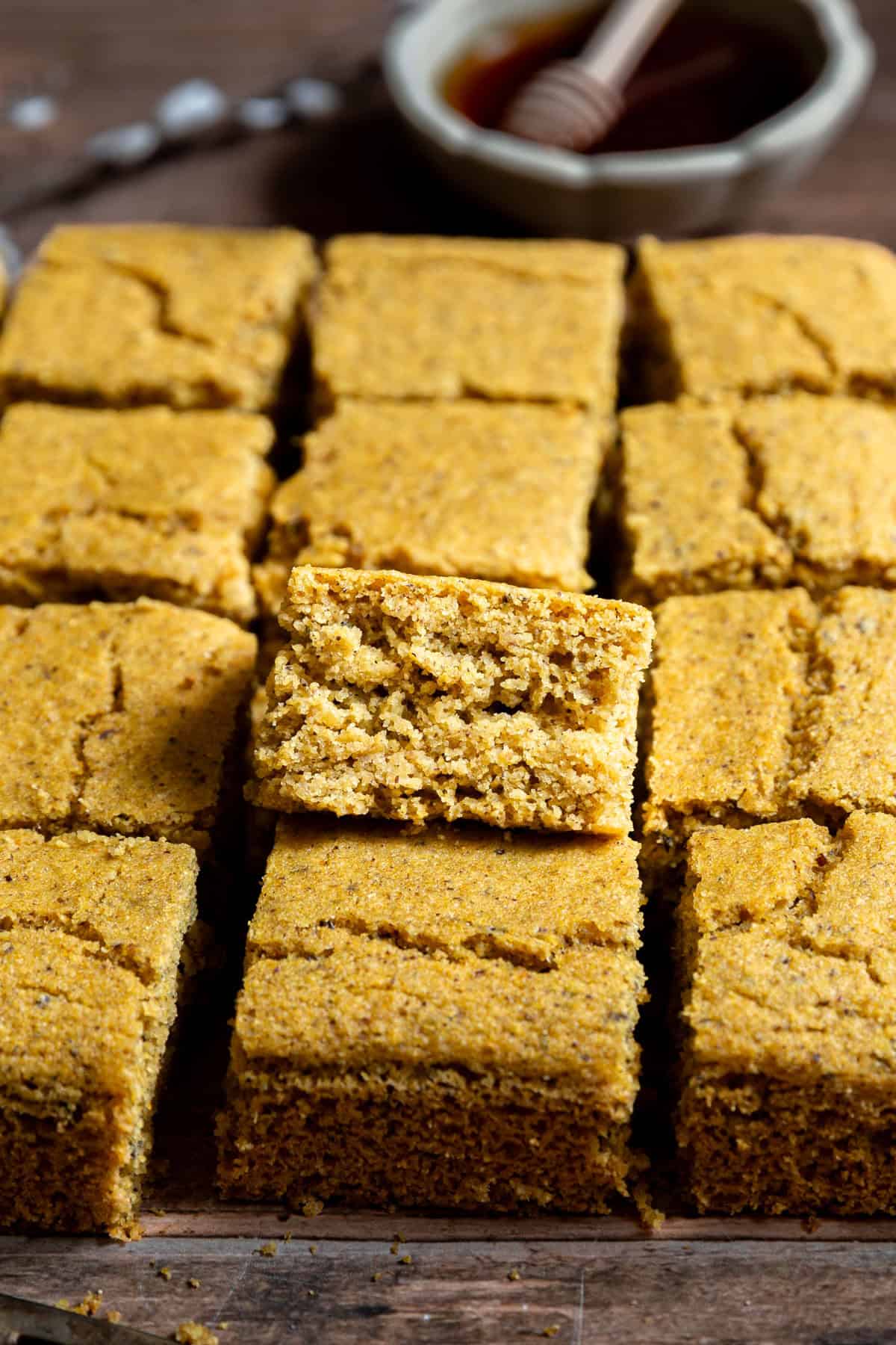 A batch of oil-free vegan cornbread, sliced into squares, with one square propped on the others, to see the texture of the bread.