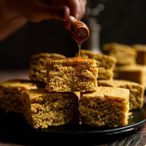Maple syrup being drizzled onto a plate of vegan cornbread.