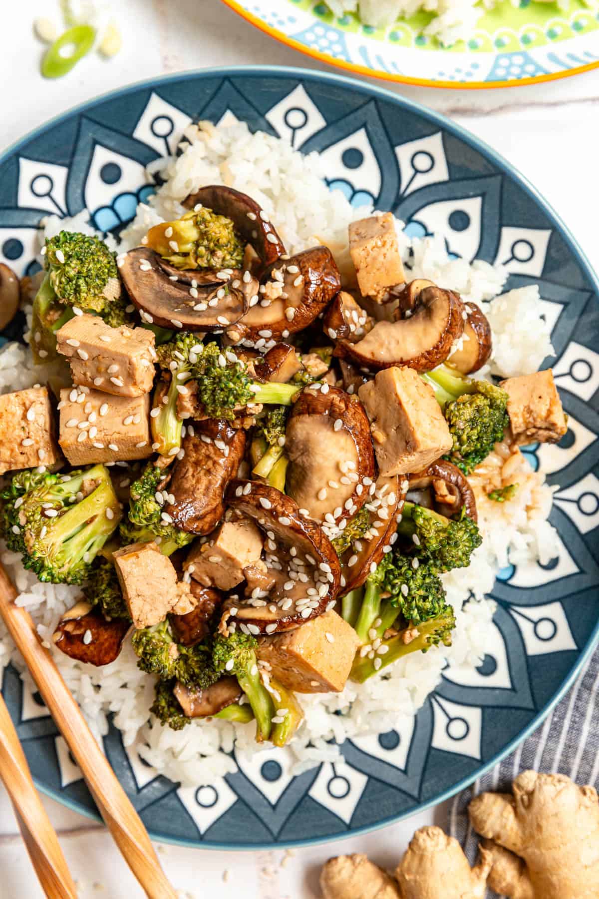 A plate of Tofu Broccoli Mushroom Stir Fry served over rice.