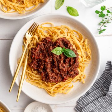 A bowl of vegan lentil bolognese on top of linguine pasta, with a garnish of basil.