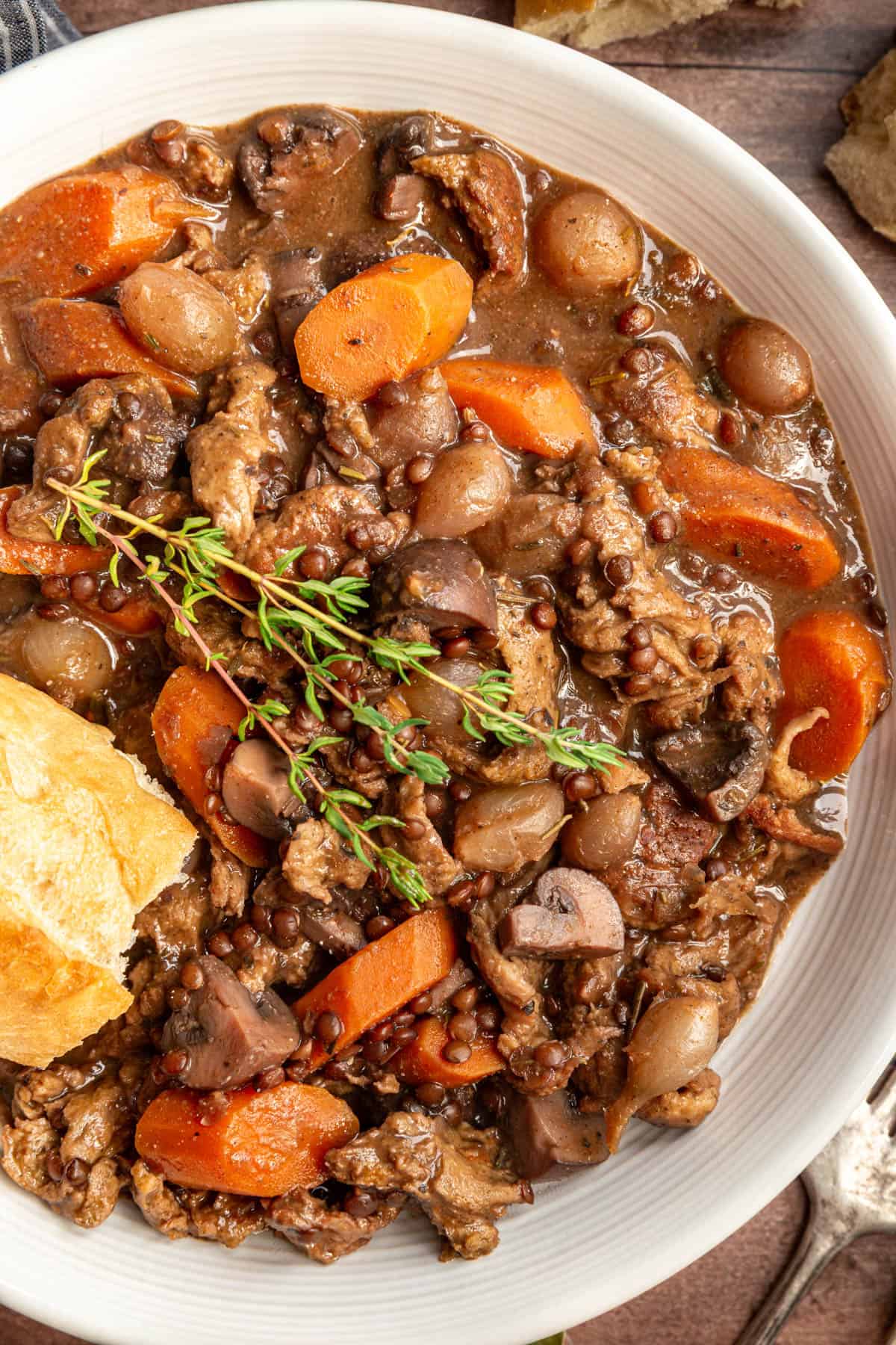 A bowl of vegan coq au vin with a garnish of thyme and a piece of French bread.