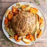 A platter of Whole Roasted Cauliflower surrounded by roasted vegetables.