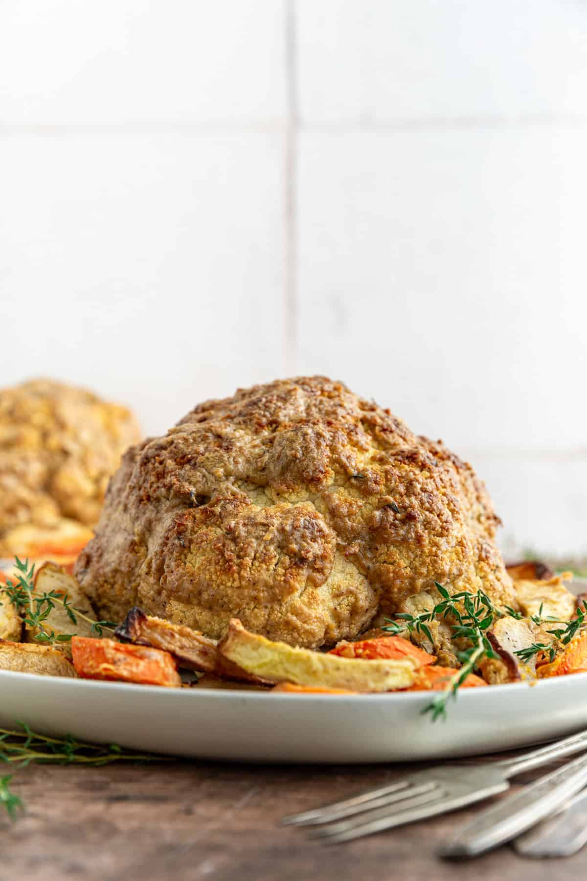 A platter of Whole Roasted Cauliflower surrounded by roasted vegetables.
