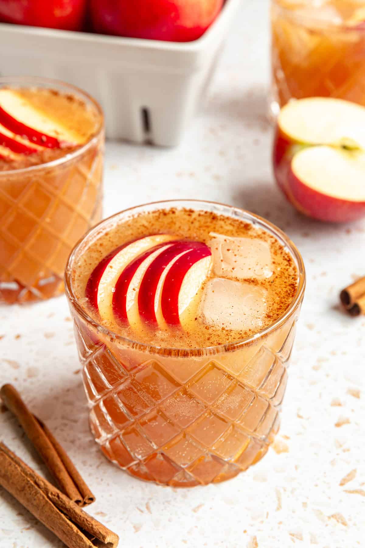 An apple mocktail in a glass, with cinnamon sticks and apples.