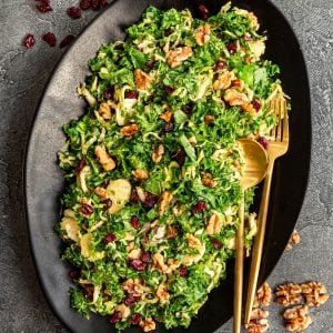 A platter of Vegan Brussels Sprouts Salad, with serving utensils, ready to serve.