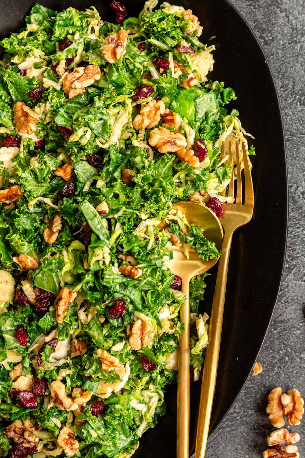 A platter of Vegan Kale Brussels Sprouts Cranberry Salad, with serving utensils, ready to serve.
