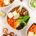 A bowl of miso soup with bok choy, garnished with carrots, nori, and a lime wedge.