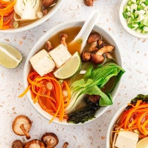 A bowl of miso soup with bok choy, garnished with carrots, nori, and a lime wedge.