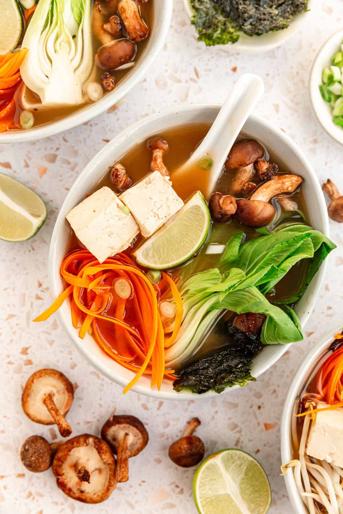 A bowl of miso soup with bok choy, garnished with carrots, nori, and a lime wedge.