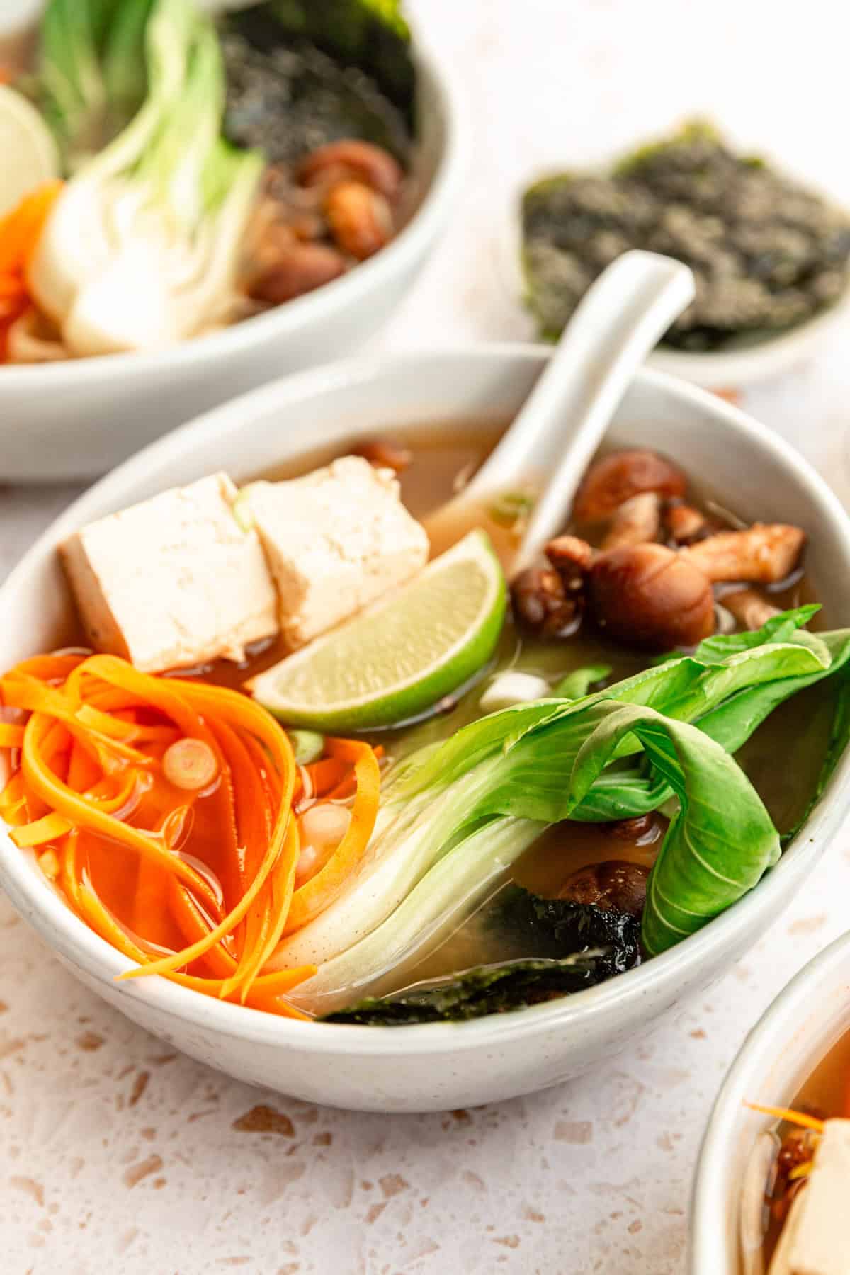 A bowl of miso soup garnished with carrots and lime wedges.