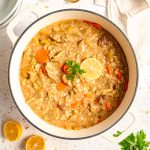 A pot of Vegan Chicken Lemon Rice Soup, with lemon wedges and parsley, ready to serve.