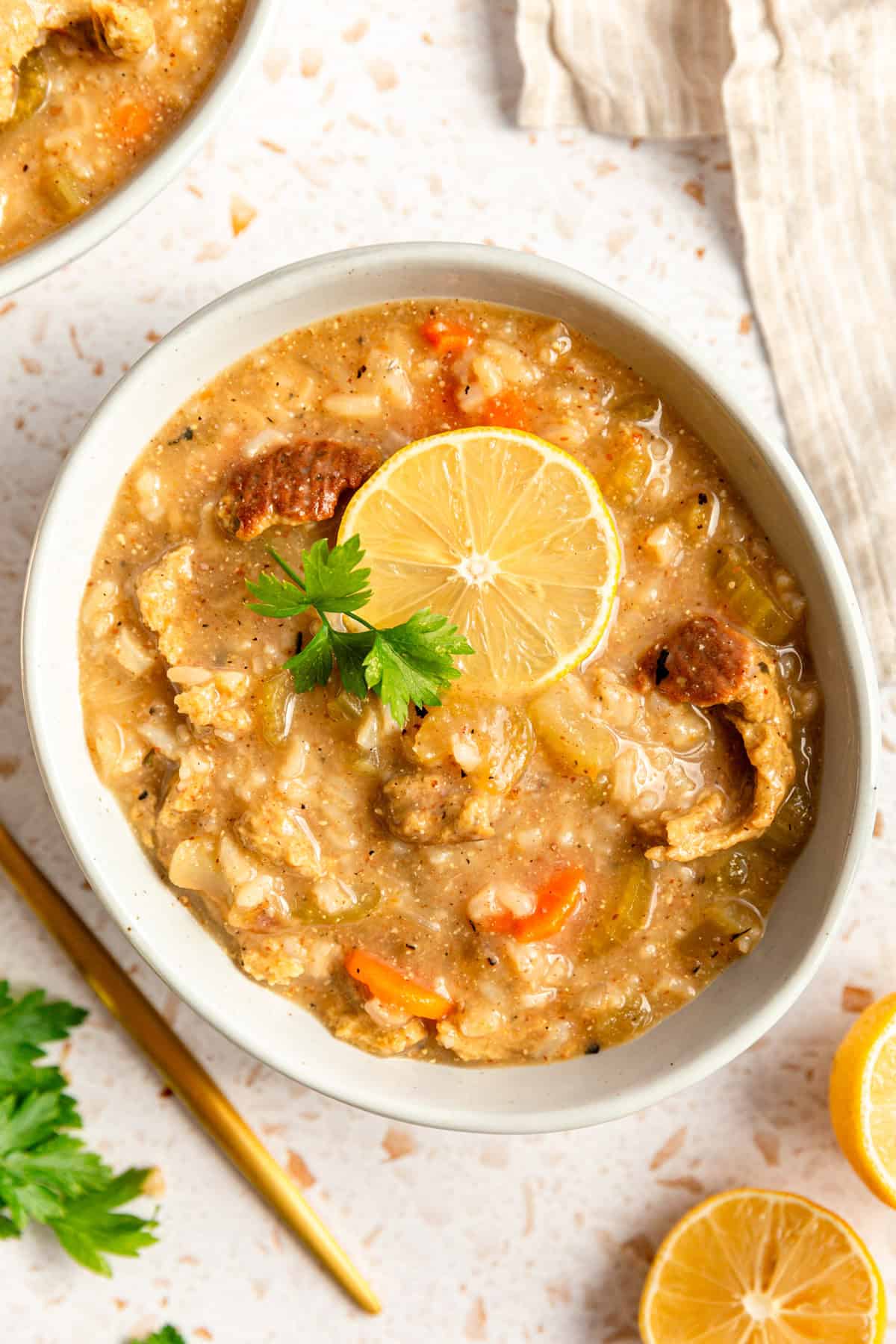 A bowl of Vegan Chicken Lemon Rice Soup, with a lemon slice and parsley.