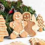 Two gingerbread men standing up, next to Christmas garland.