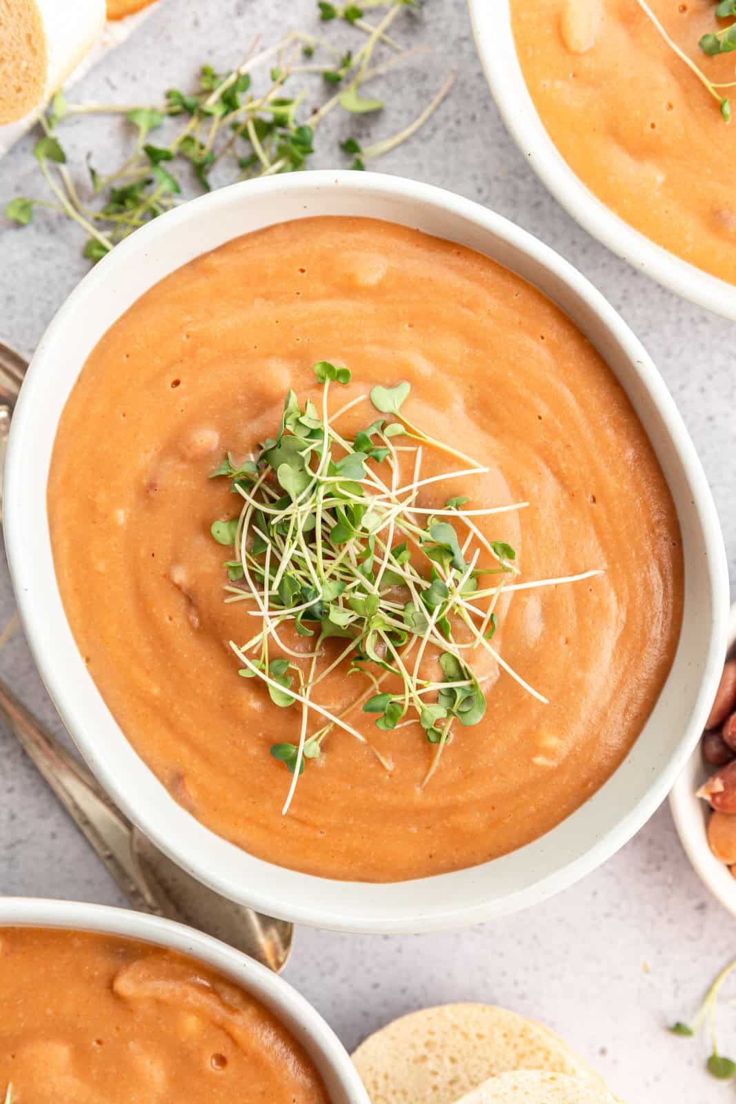 Three bowls of pinto bean soup with bread and microgreens.