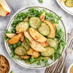 A plate of apple pear cucumber salad served over arugula.