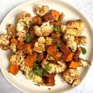 A plate of balsamic roasted cauliflower and sweet potatoes garnished with parsley.