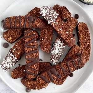 A plate of plant-based chocolate coconut biscotti, decorated with chocolate and coconut flakes.
