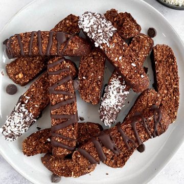 A plate of plant-based chocolate coconut biscotti, decorated with chocolate and coconut flakes.