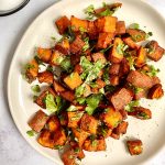 A plate of date glazed spicy sweet potatoes garnished with cilantro.