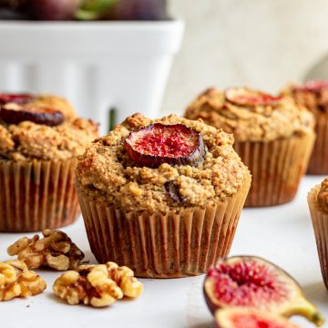 A fresh fig muffin on a countertop with walnuts and figs.