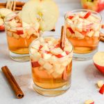 Three apple cider spritzers, garnished with apple slices and cinnamon sticks.