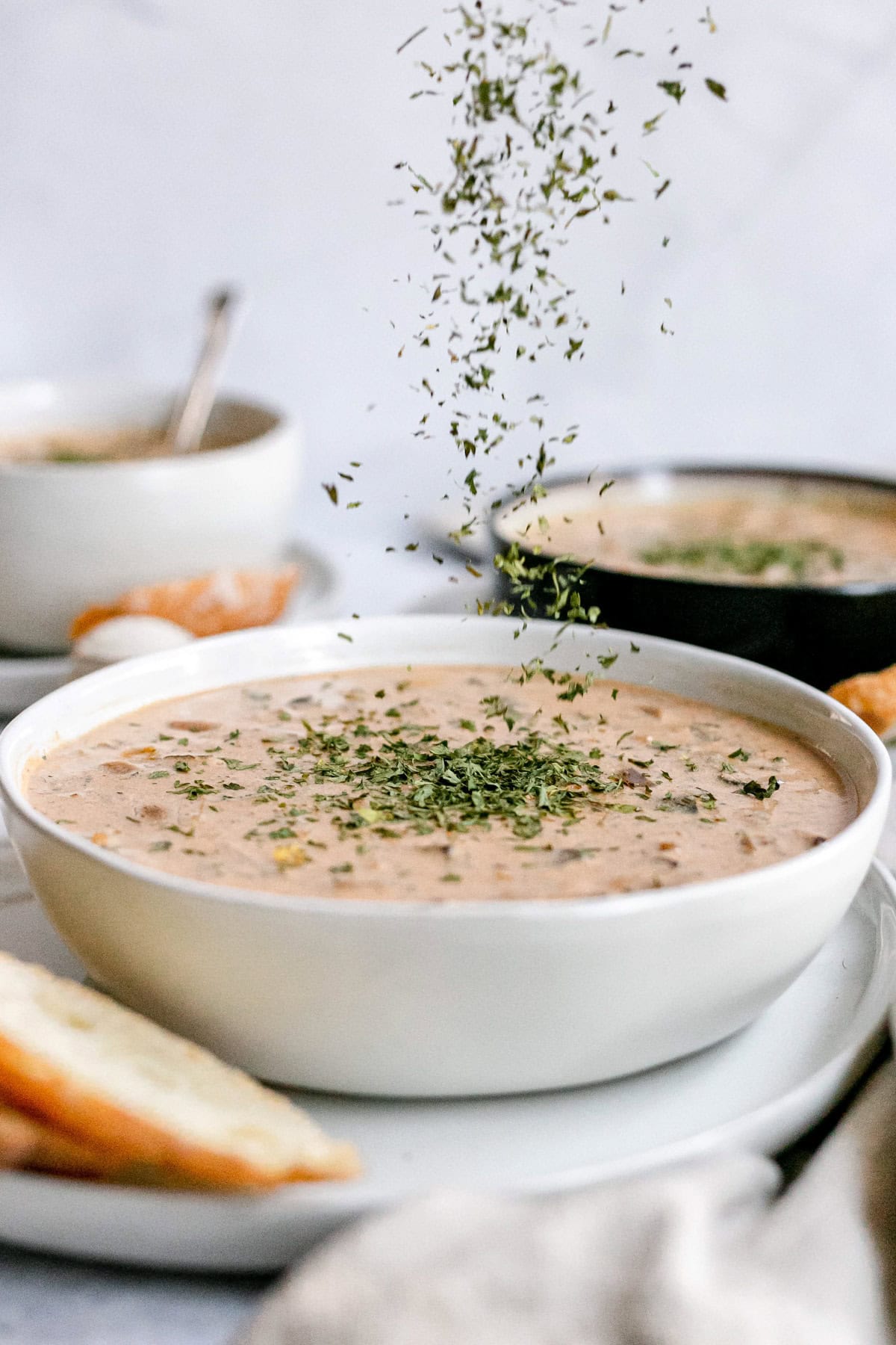 A bowl of Hungarian mushroom soup being sprinkled with parsley.