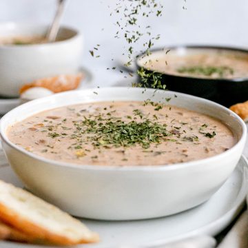 A bowl of Hungarian mushroom soup being sprinkled with parsley.