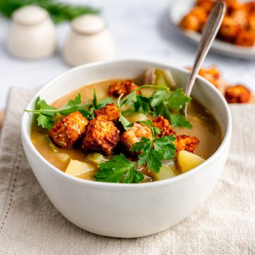 A bowl of plant-based Hungarian potato soup topped with tempeh and garnished with parsley.