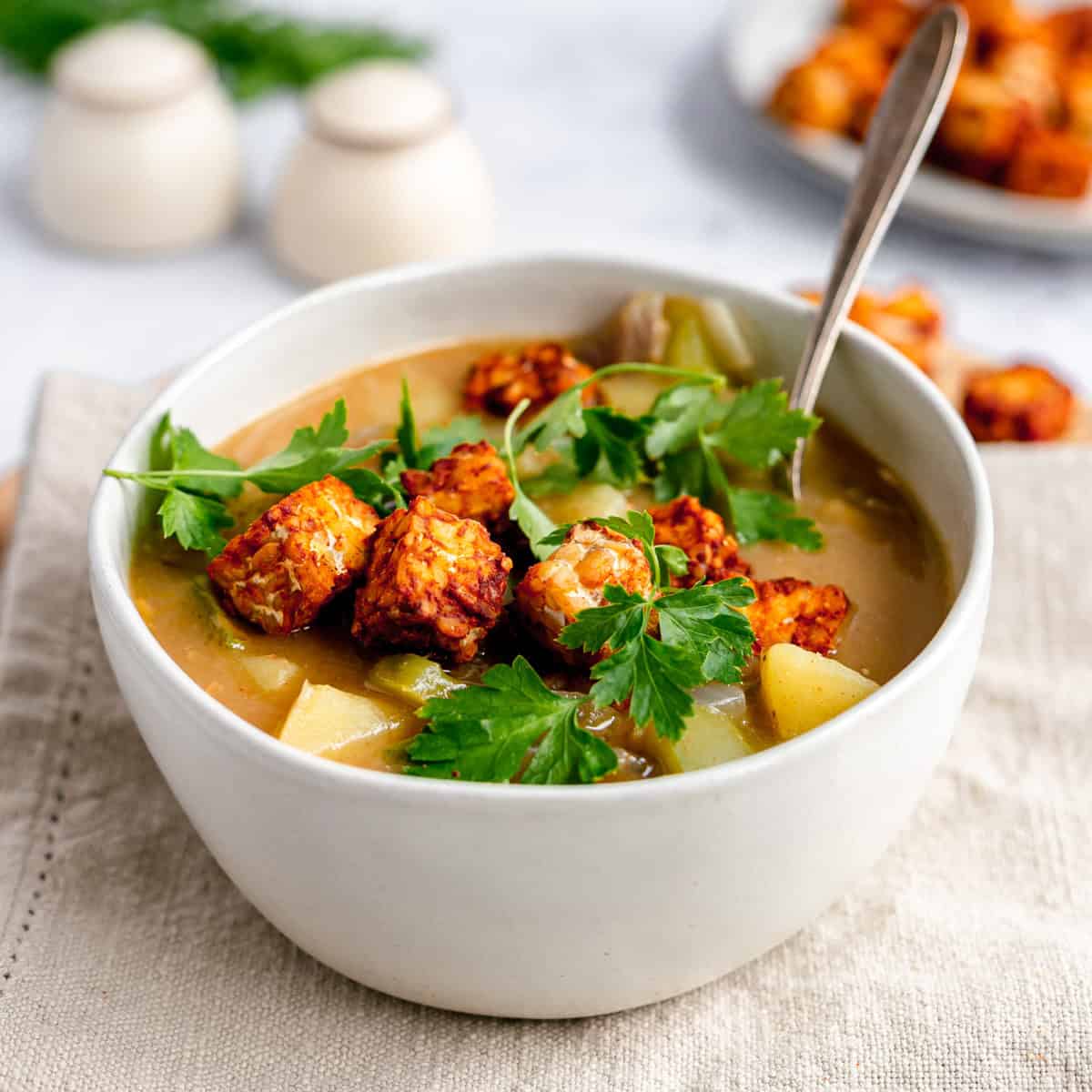 A bowl of plant-based Hungarian potato soup topped with tempeh and garnished with parsley.