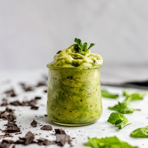 A jar of mint chocolate chip soft serve, garnished with a sprig of mint.