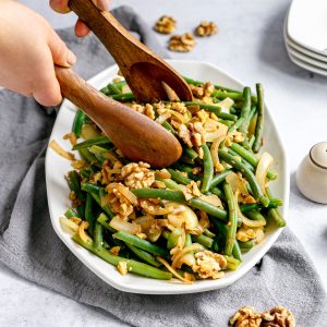 A person scooping a platter of oil-free green beans.