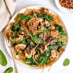 A plate of spinach mushroom pasta, with a fork, ready to serve.